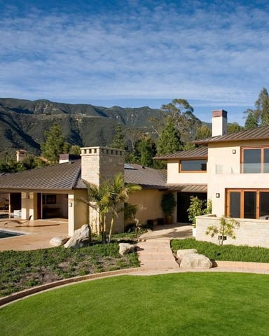 Modern two-story house with curved pool, manicured lawn, and mountain backdrop