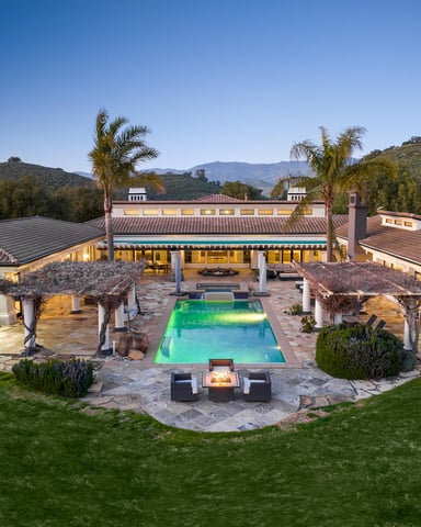 Illuminated pool and fire pit at dusk with Santa Ynez hills in the background