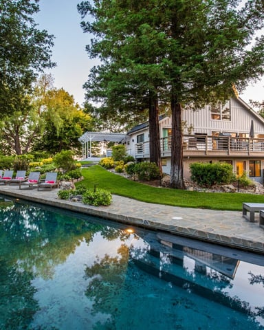 Modern house with pool, lounge chairs, and manicured lawn surrounded by tall trees