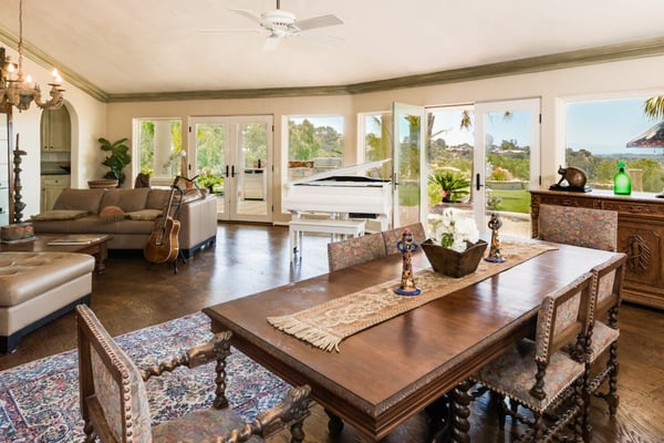 Open-plan living and dining room with wood floors, multiple glass doors opening to terrace, and hillside views