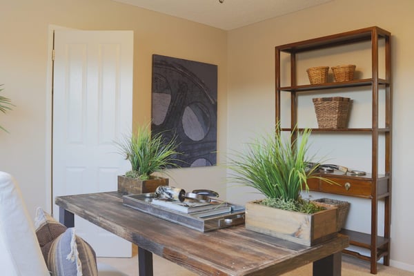 Bedroom with wooden desk, potted plants, abstract artwork, and wooden shelving unit with woven baskets