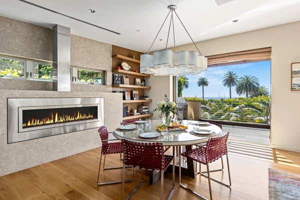 Open-plan living and dining room with wood floors, multiple glass doors opening to terrace, valley views, and decorative furnishings.